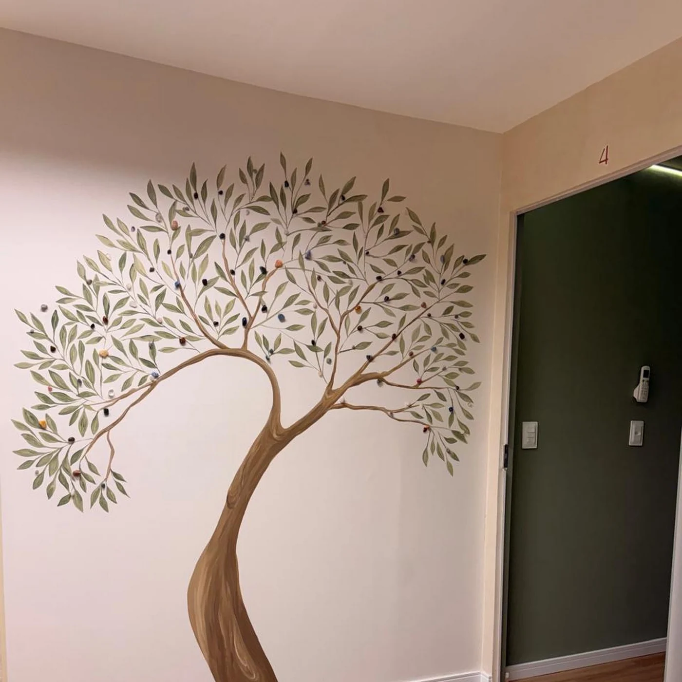 A oliveira pintada à mão na parede da clínica, ao lado da porta verde do consultório